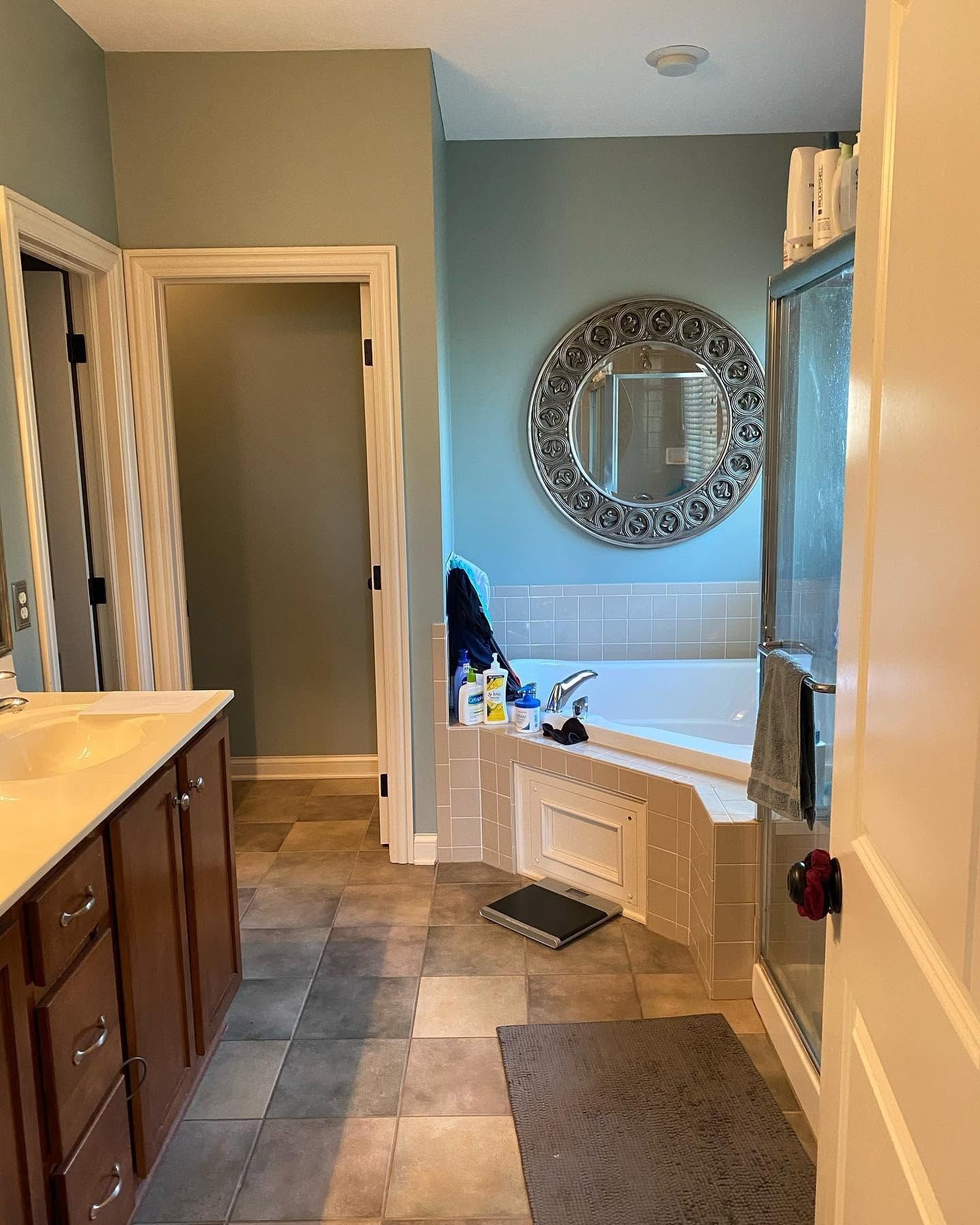 The bathroom before: green walls, dark wood vanity and a tiled corner tub