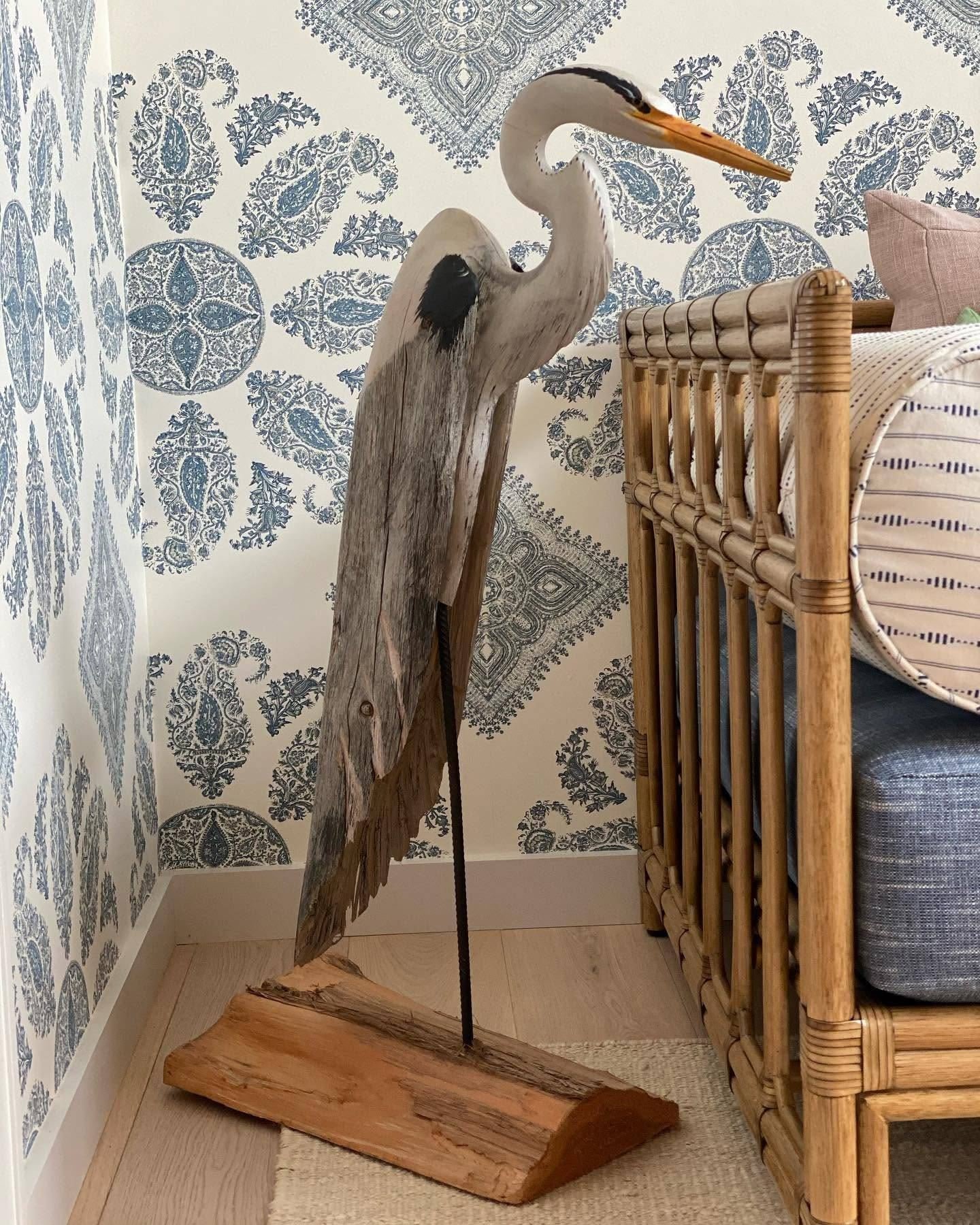 Carved wooden heron beside a rattan daybed against blue paisley wallpaper