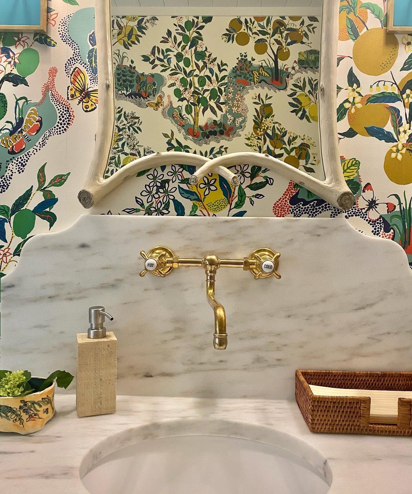 Powder room with citrus-print wallpaper, marble backsplash and a brass wall faucet