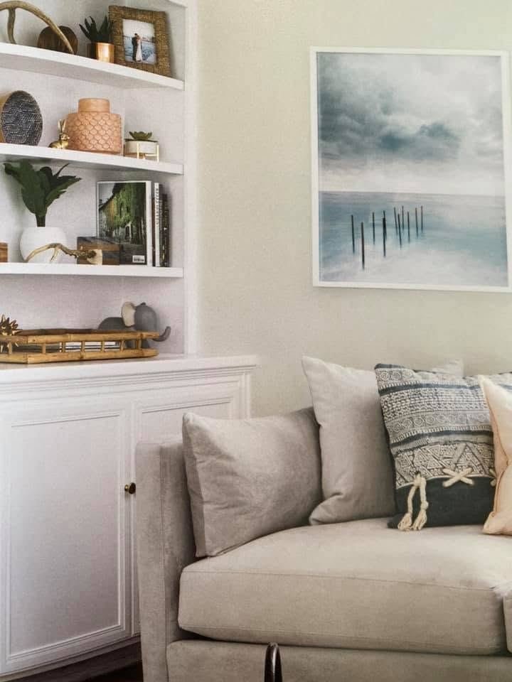 White built-in shelves beside a sofa and a misty seascape print