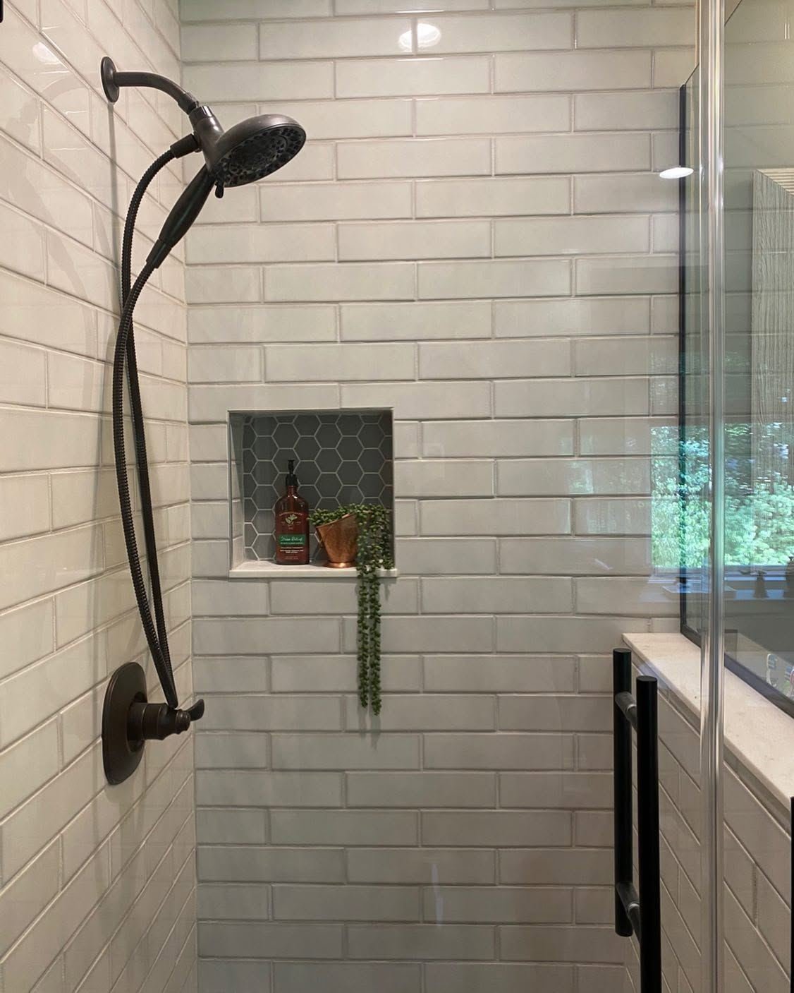 Tiled walk-in shower with bronze fixtures and a hexagon-tile niche