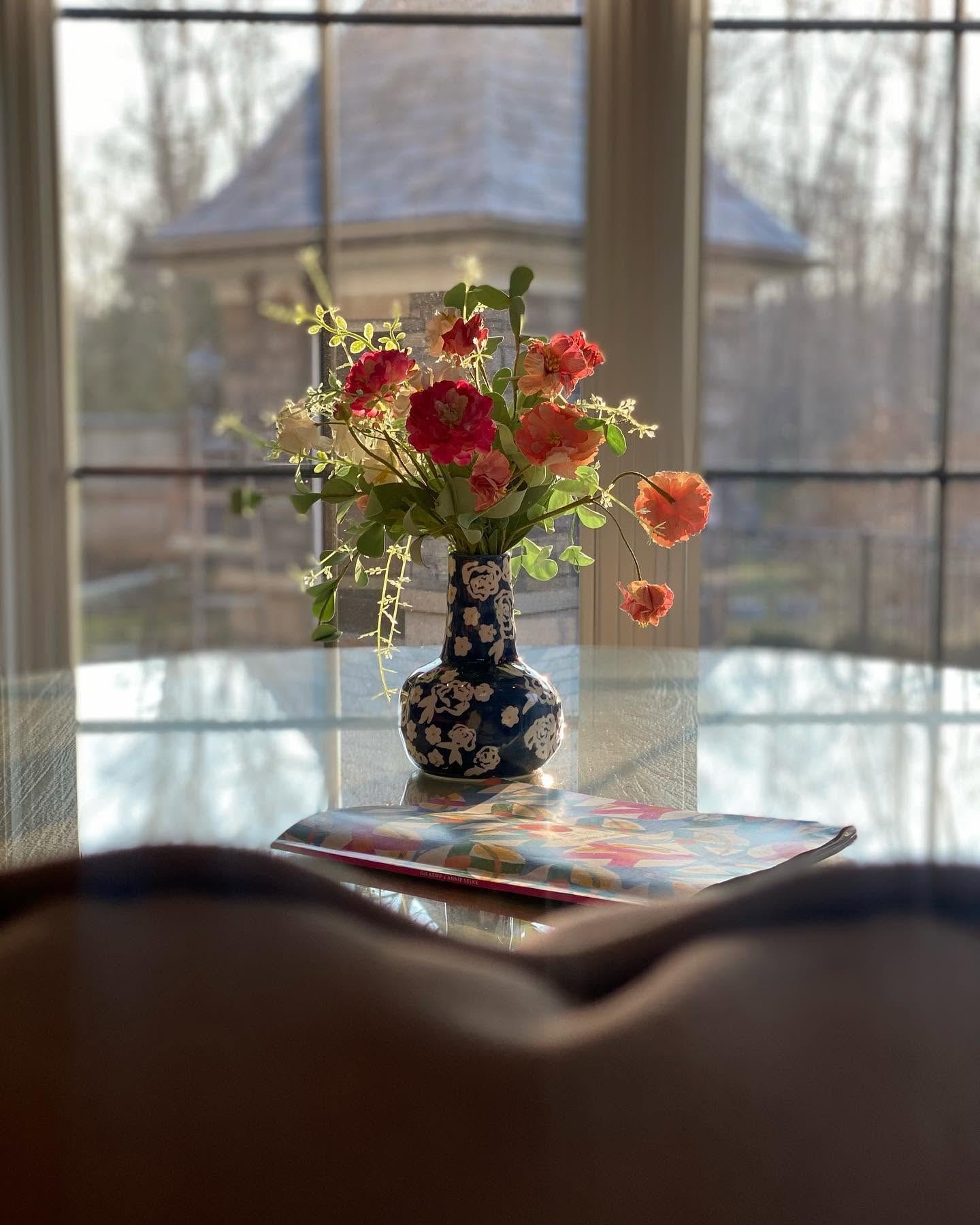 Coral and pink flowers in a blue and white vase by a window